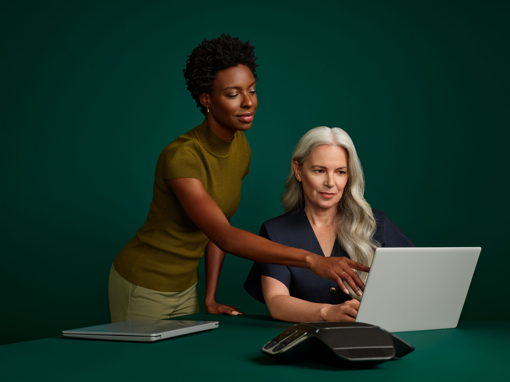Portrait of a female coding director and hospital administrator reviewing an online document at a desk computer on a dark green background.