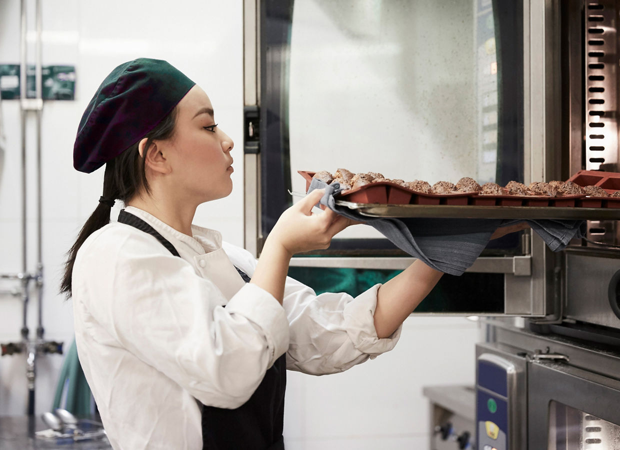Frau stellt Tablett in den Dampfofen
