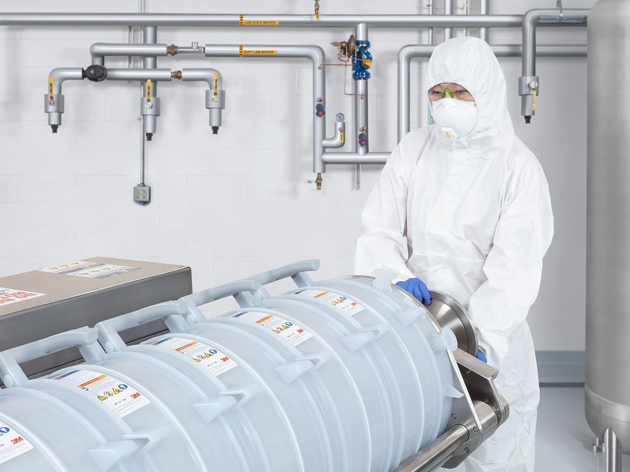 Bioprocessing technician in white cleanroom suit adjusting large piece of equipment.