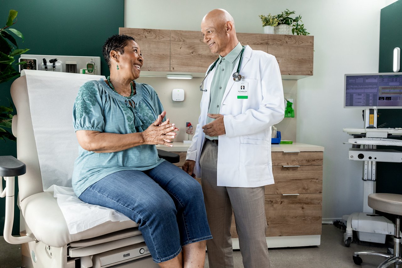 Paciente femenina madura riendo e interactuando con un doctor de atención primaria masculino en una sala de examen.