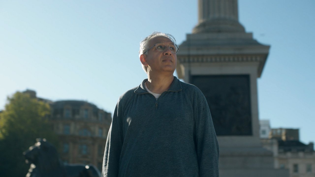 A man stands in front of a monument with a column and statue on a clear, sunny day.