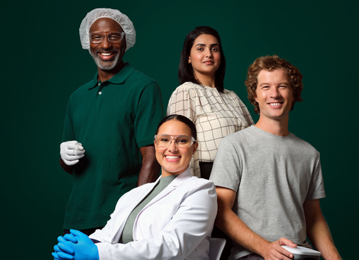 Foto eines Unternehmensmitarbeiters. Eine Anwendungsingenieurin mit Brille und blauen Handschuhen, ein HISD-Mitarbeiter, der auf einem Stuhl sitzt und ein Softwaregerät hält, ein männlicher OCSD-Fertigungsmitarbeiter in einem Haarnetz mit Aligner-Etui, der neben einer MSD-Mitarbeiterin steht.