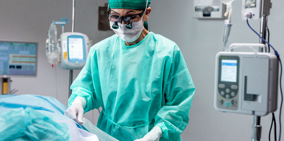A female surgeon applies dressing on a patient lying on an operating table obscured by the camera angle.