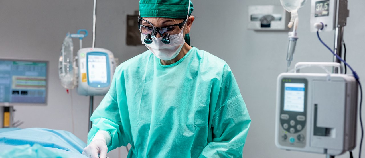 A female surgeon applies dressing on a patient lying on an operating table obscured by the camera angle.