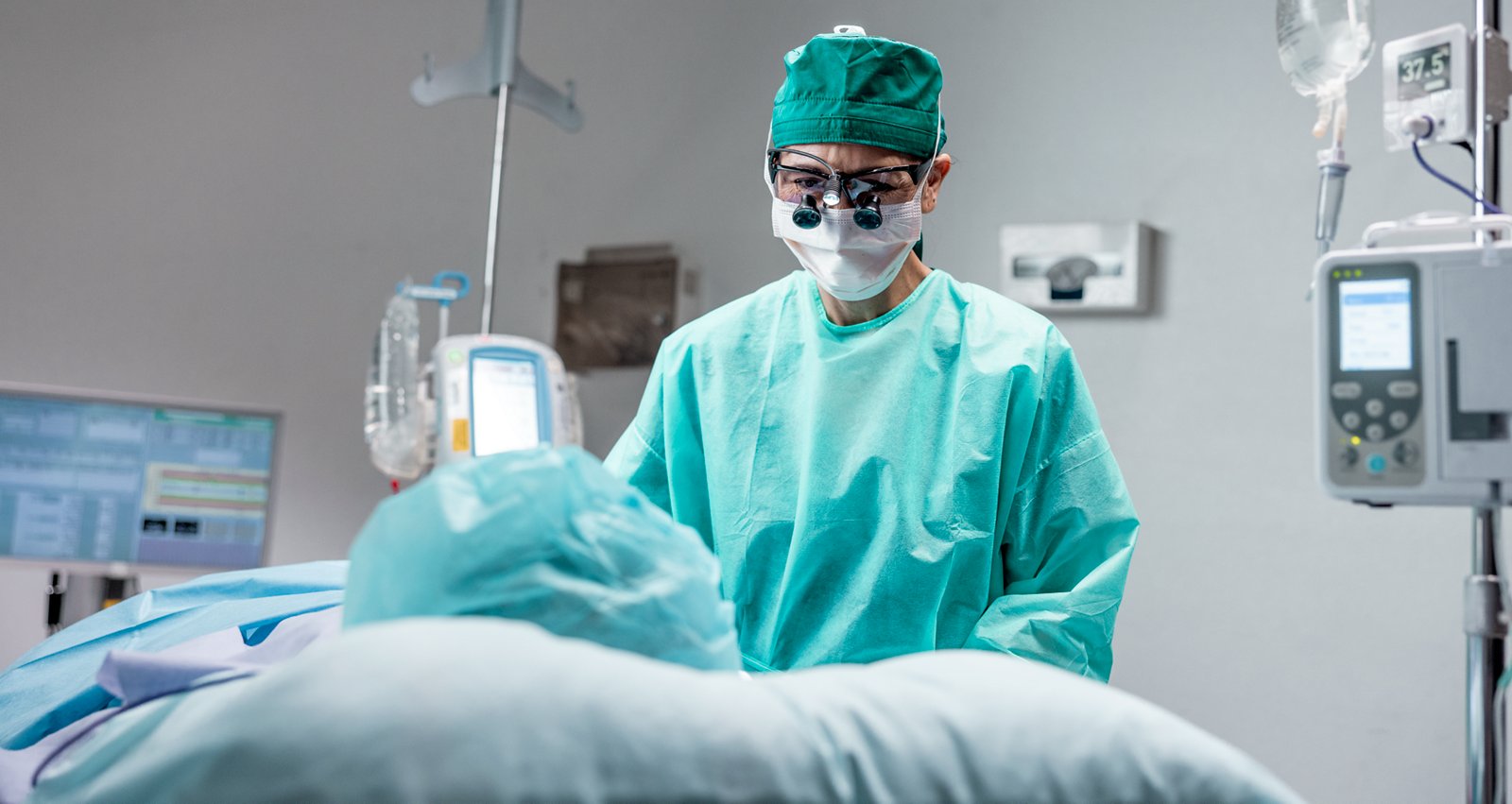 A female surgeon stands over a patient lying on an operating table in the operating room.