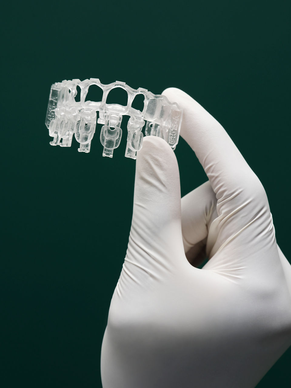 White gloved hand holding up a dental 3M Filtek Matrix on a dark green background.