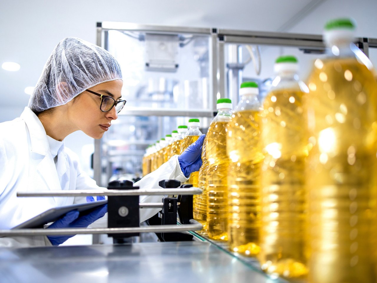 Female worker inspects bottles of cooking oil on conveyor belt