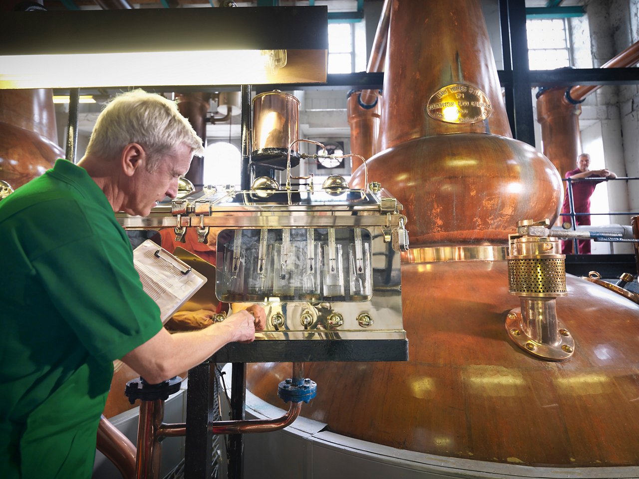 Worker inspecting pure whisky flowing from the stills in the distillery