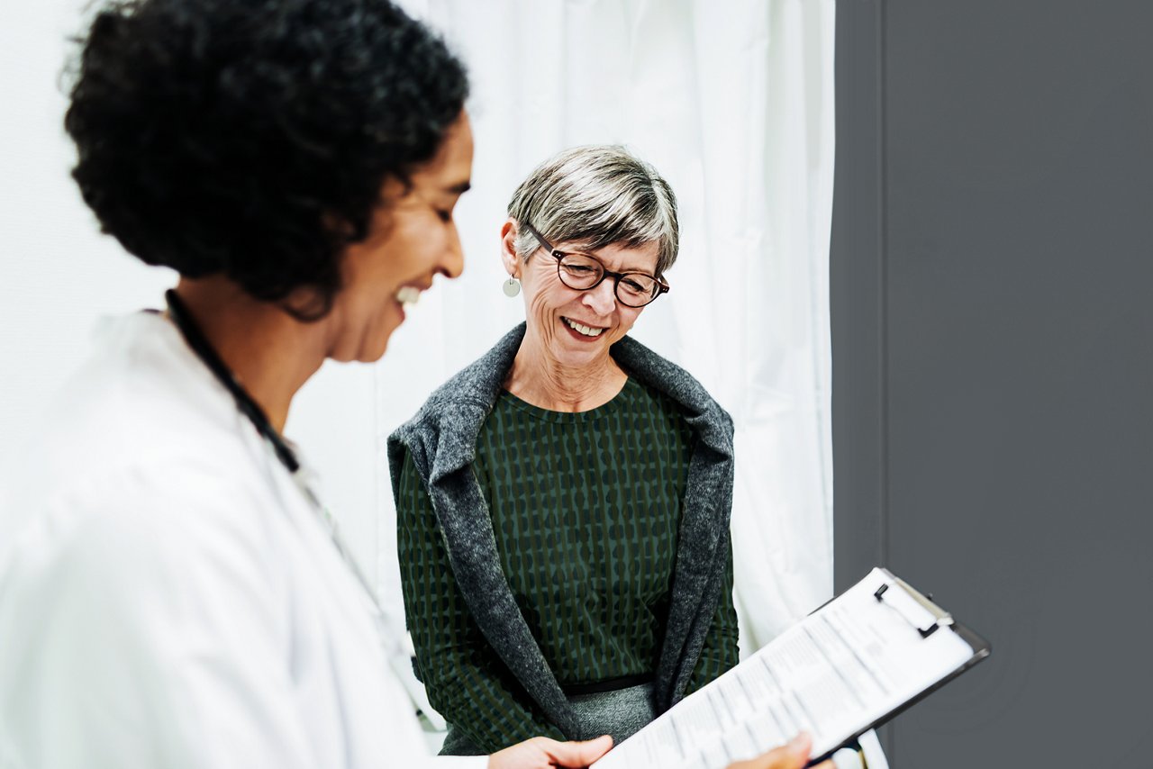 A smiling physician talking with a patient while looking at clipboard