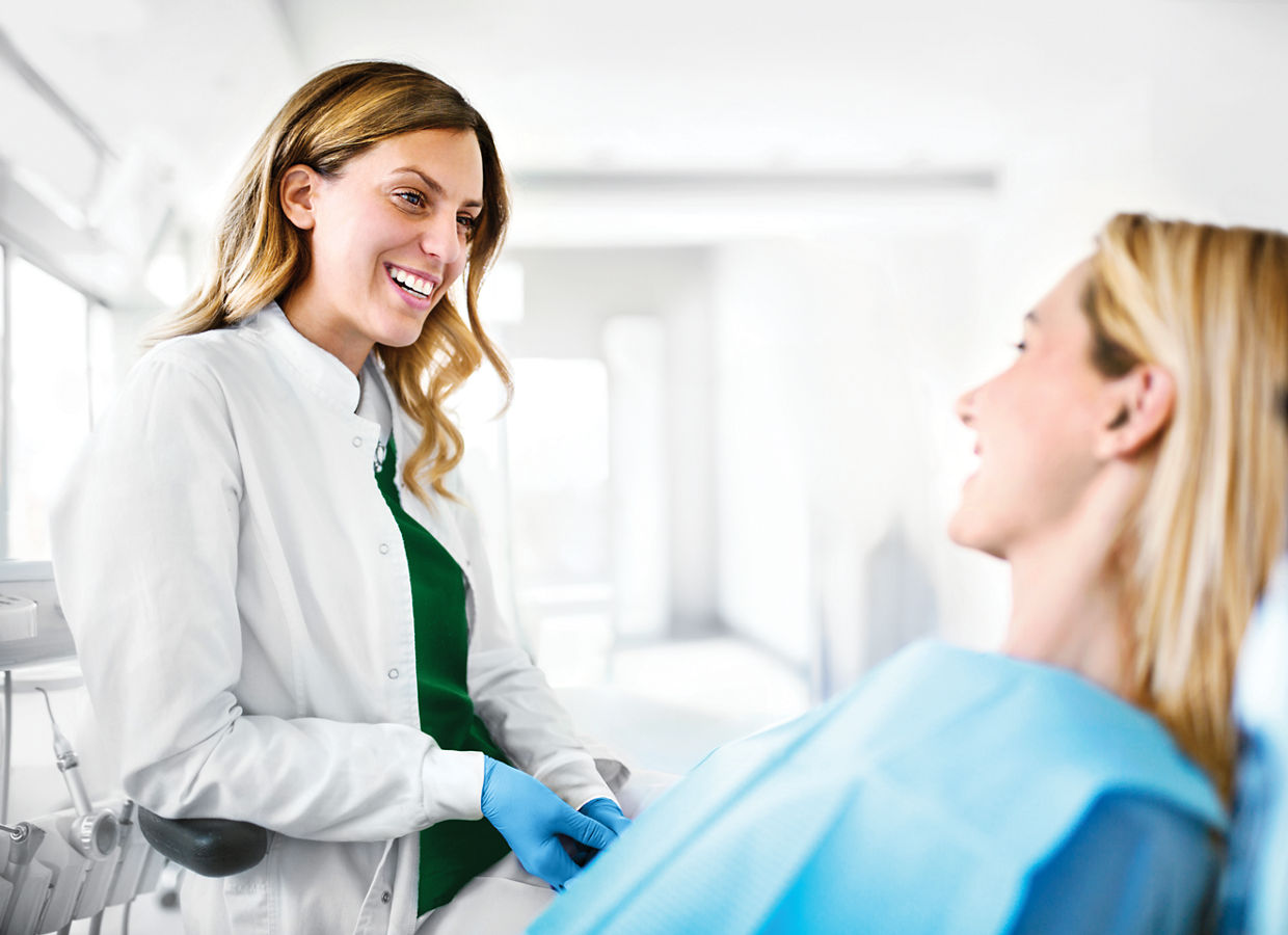 Young cheerful female dentist listening issues that female patient having with her teeth.