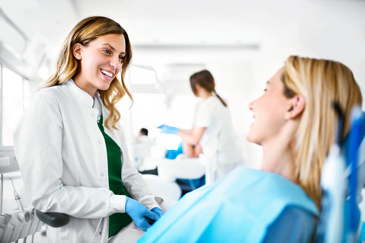 Young cheerful female dentist listening issues that female patient having with her teeth.