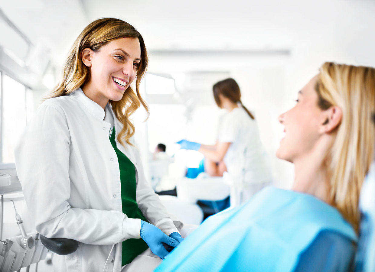 Young cheerful female dentist listening issues that female patient having with her teeth.