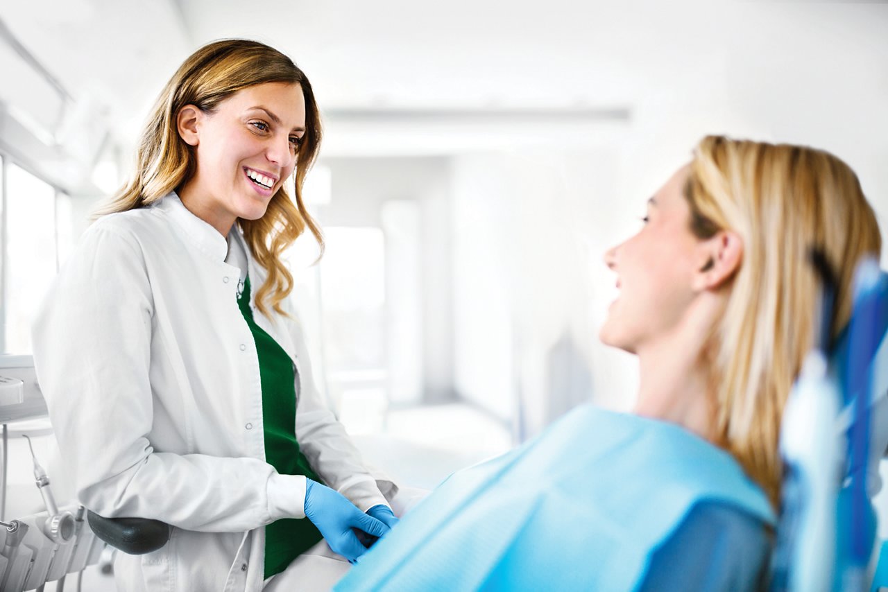 Young cheerful female dentist listening to issues that female patient having with her teeth. 