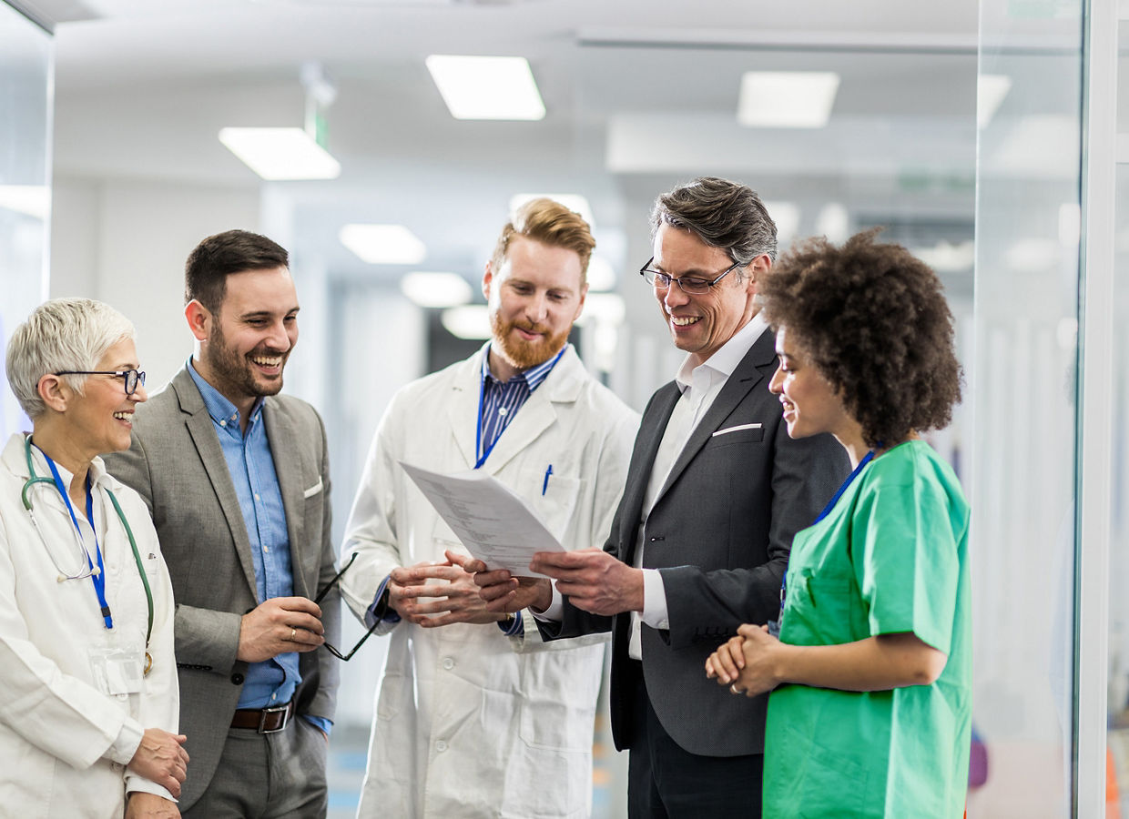 A group of clinicians and business leaders looking at a document and smiling.