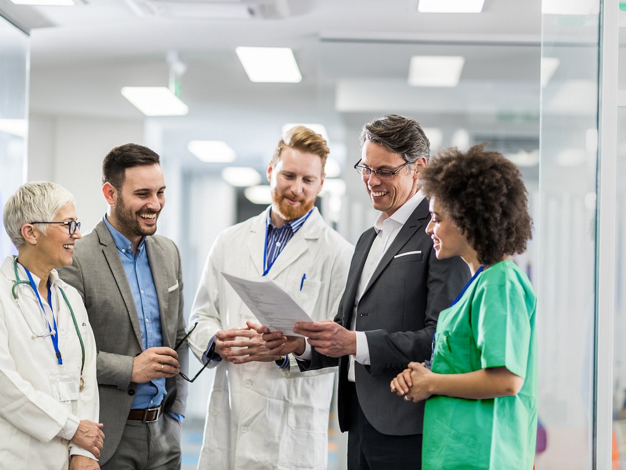 A group of clinicians and business leaders looking at a document and smiling.