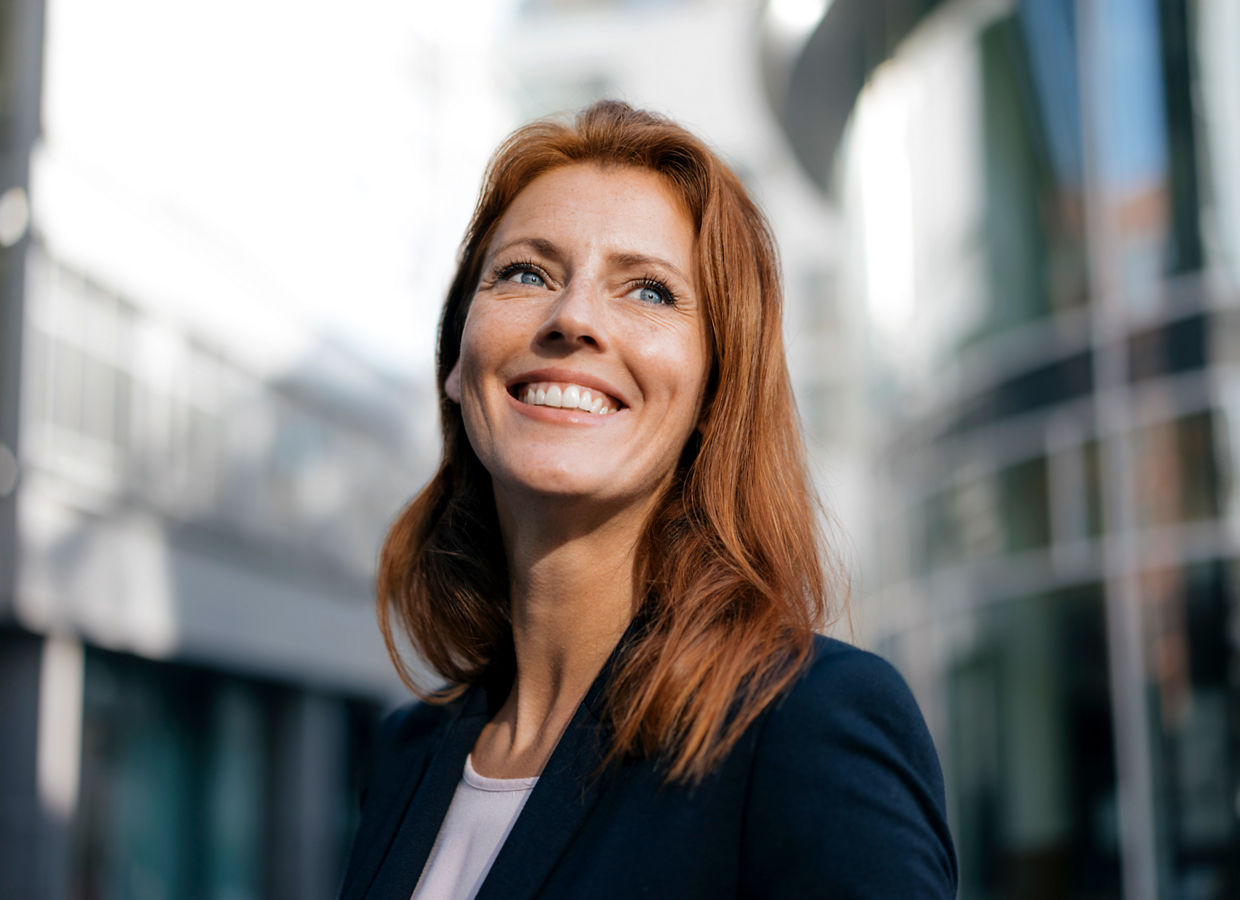 A smiling woman dressed in a business suit standing outdoors in the city.