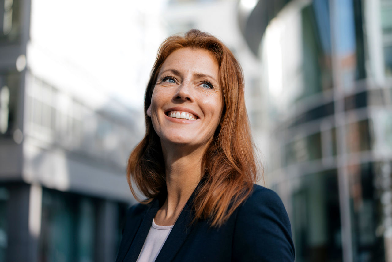 A smiling woman dressed in a business suit standing outdoors in the city.