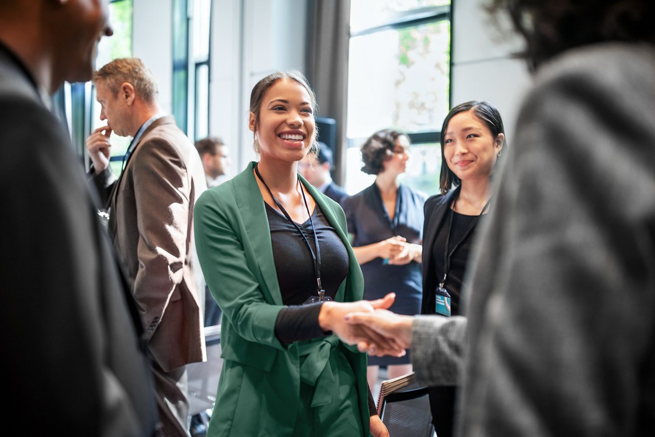 Group of professionals at a networking event with one woman introducing herself to another.