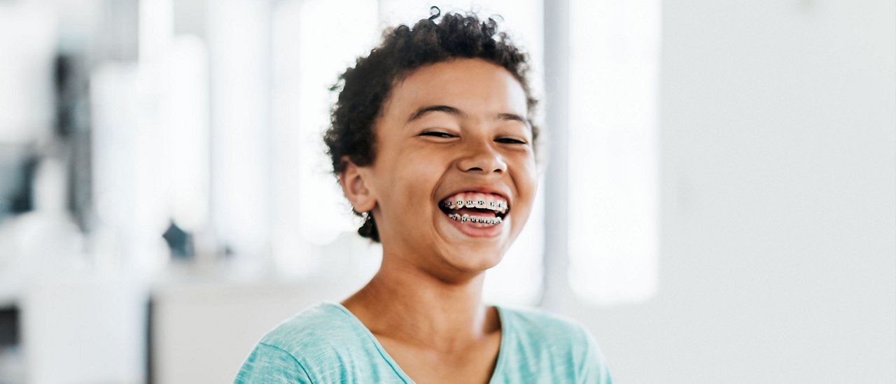 A young boy with braces on his teeth laughing.