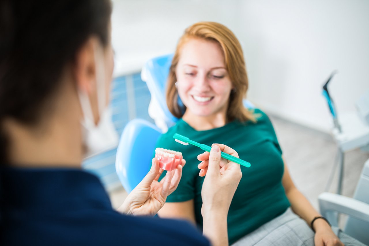 A dental hygienist showing a female patient how to brush her teeth