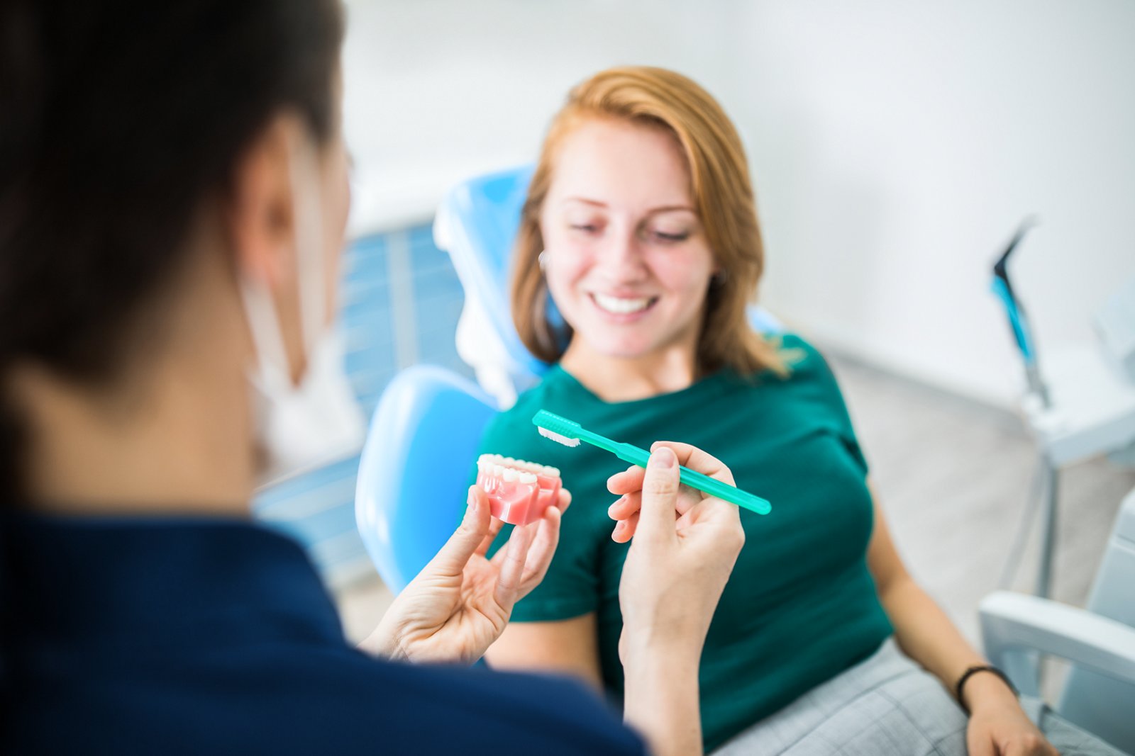 A dental hygienist showing a female patient how to brush her teeth