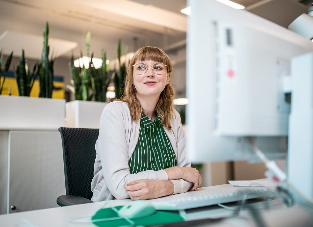 A woman at a desk looking away from her computer with a slight smile.