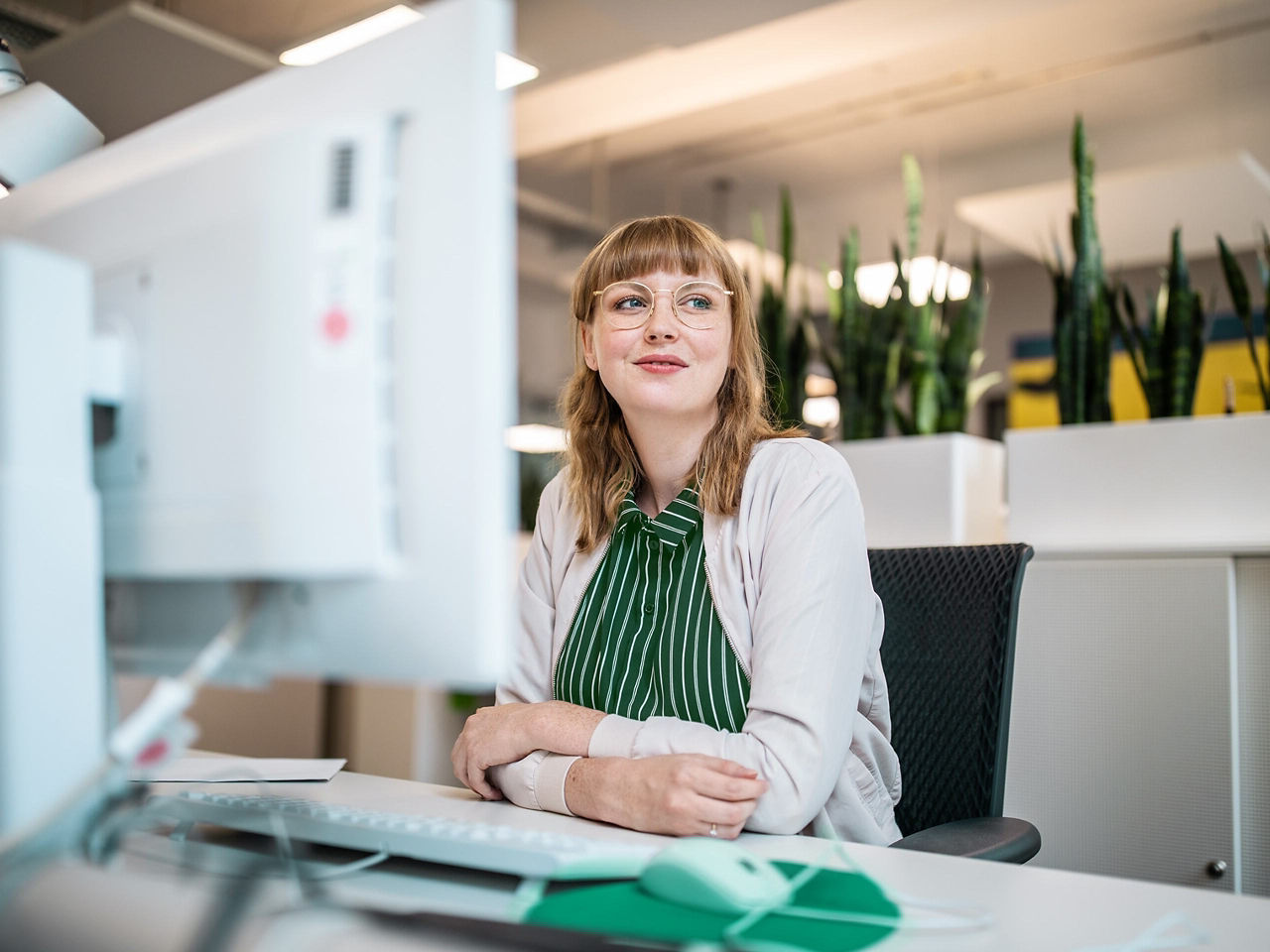 A woman at a desk looking away from her computer with a slight smile.
