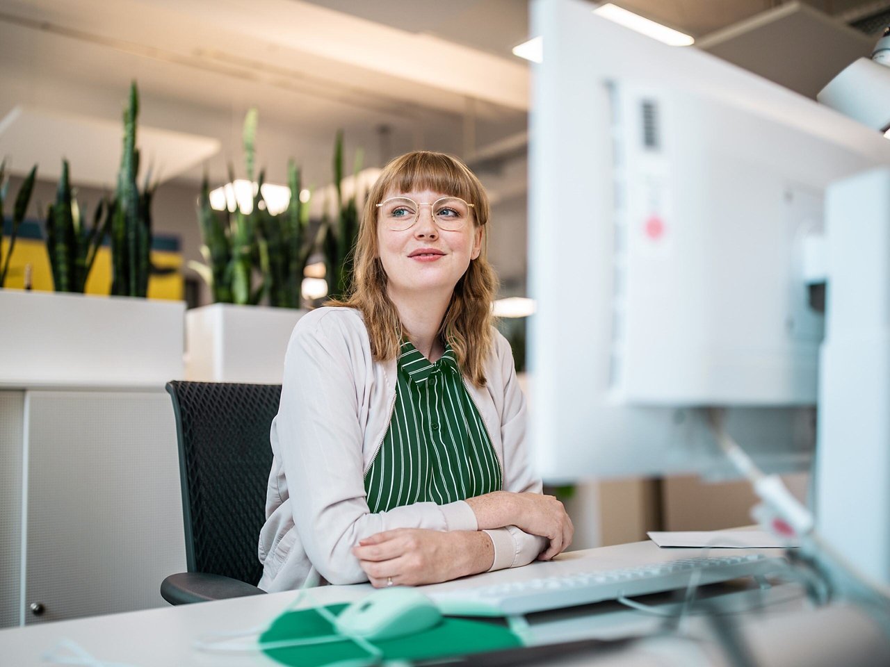 A woman at a desk looking away from her computer with a slight smile.