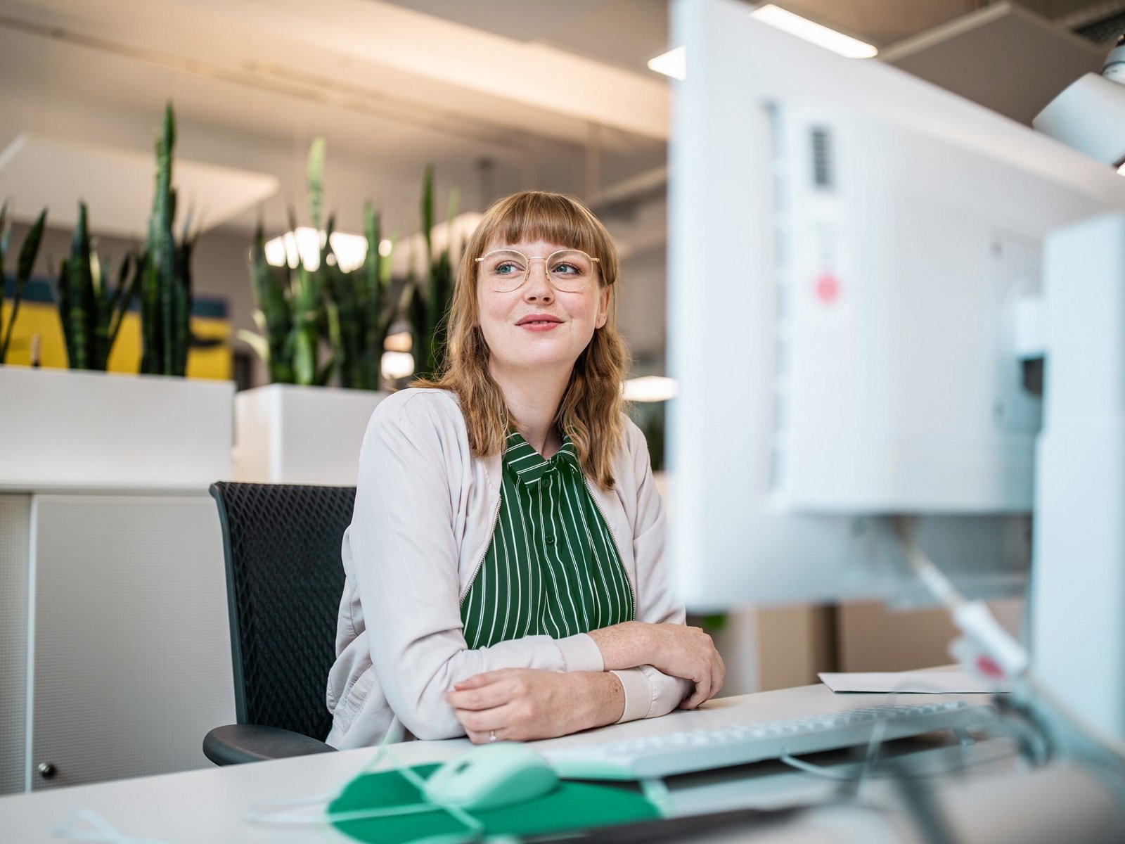 A woman at a desk looking away from her computer with a slight smile.
