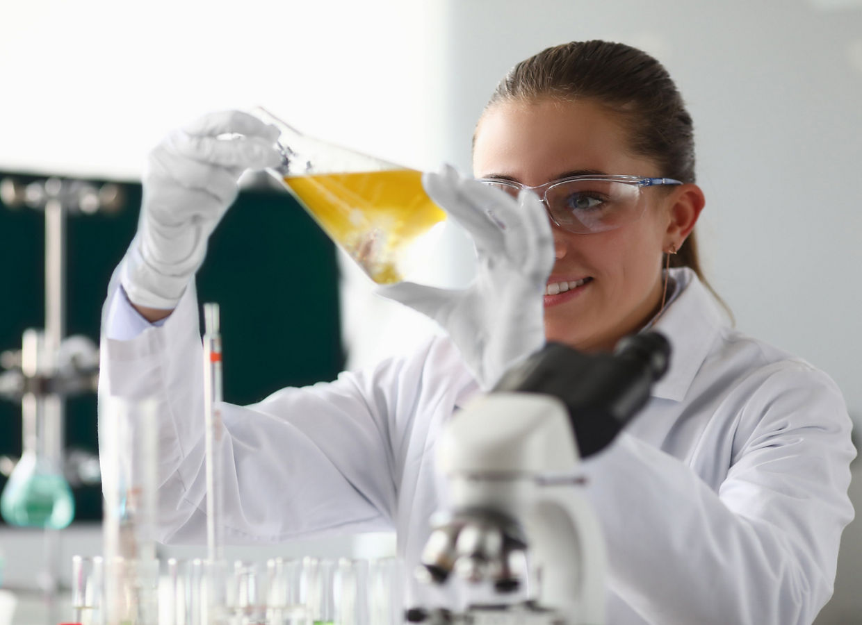 一位科学家戴着安全护目镜、手套和实验服，在实验室检查一个装有液体的烧杯。