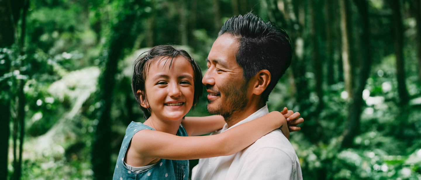 Padre che tiene la figlia tra le braccia circondata da una foresta lussureggiante.