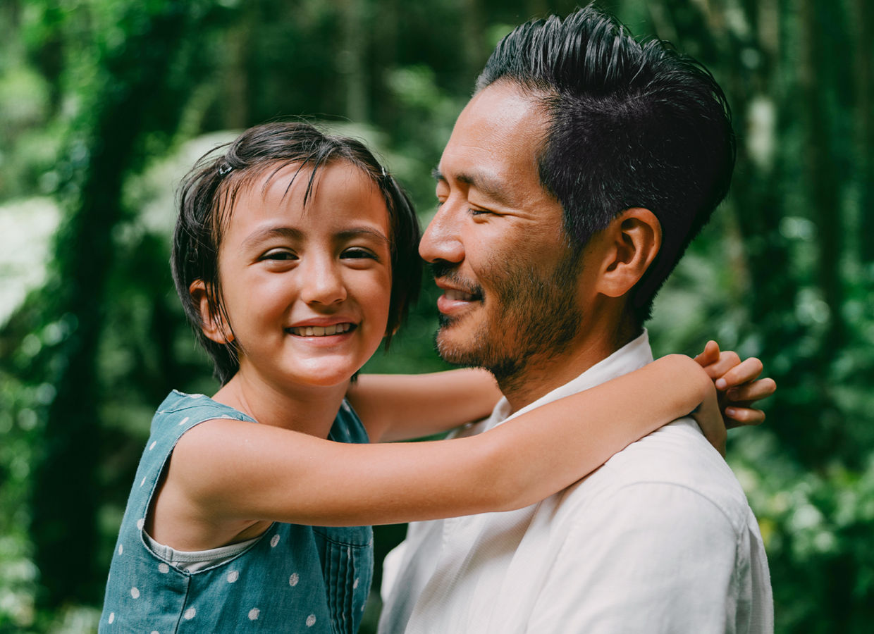 Padre che tiene la figlia tra le braccia circondata da una foresta lussureggiante.