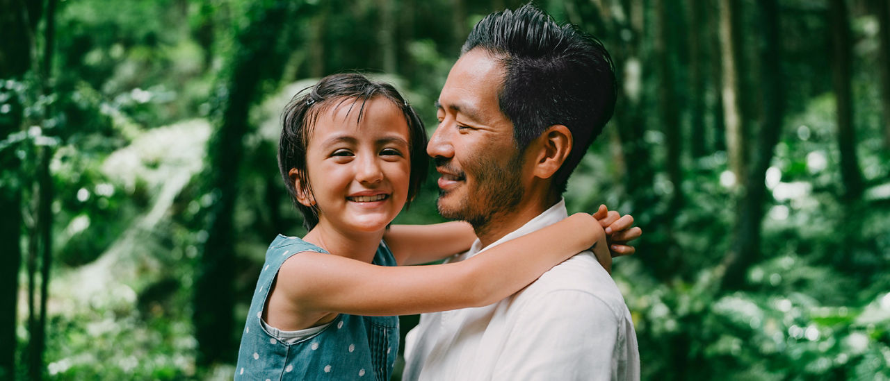 A man holds and looks lovingly at his young child, who has her arms around her father’s neck, smiling.