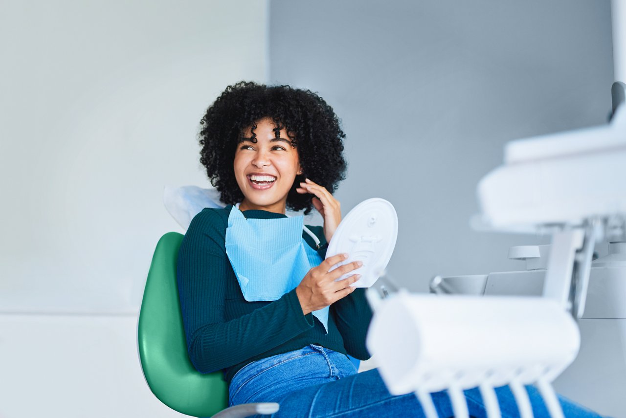 Smiling young girl sitting in a dental chair with a mirror in her hand