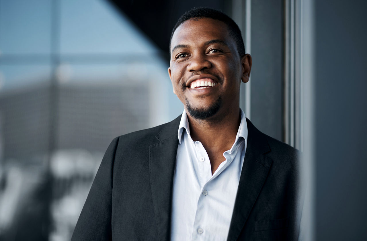 A businessman leaning against a wall smiling.