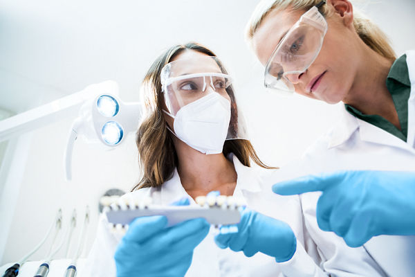 Two female oral care specialists wearing lab coats and safety googles interacting with dental products.