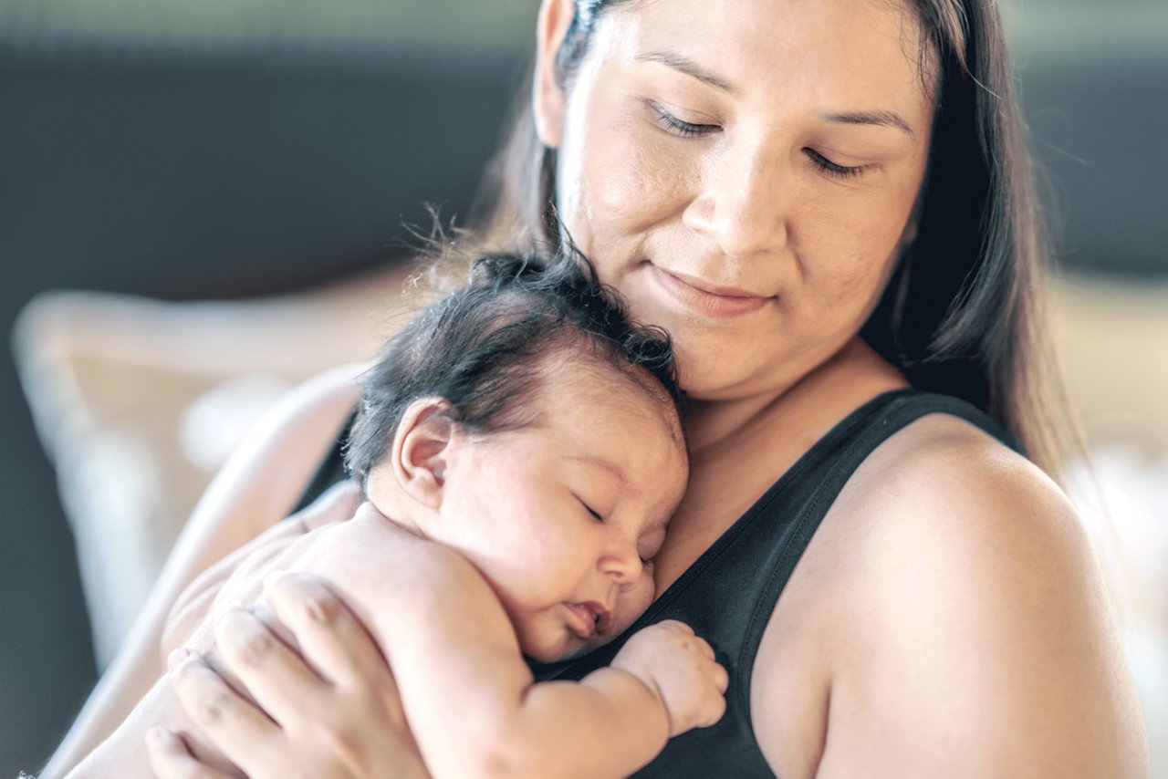 A mother holding her baby close to her body.