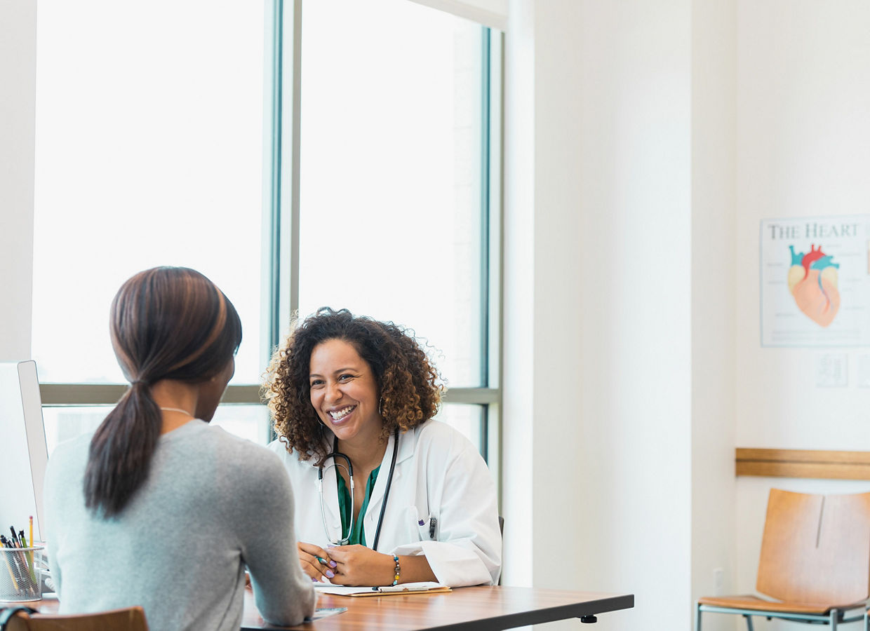 A clinician sitting at a table smiling at a patient. On the wall in the room is a poster of the human heart.