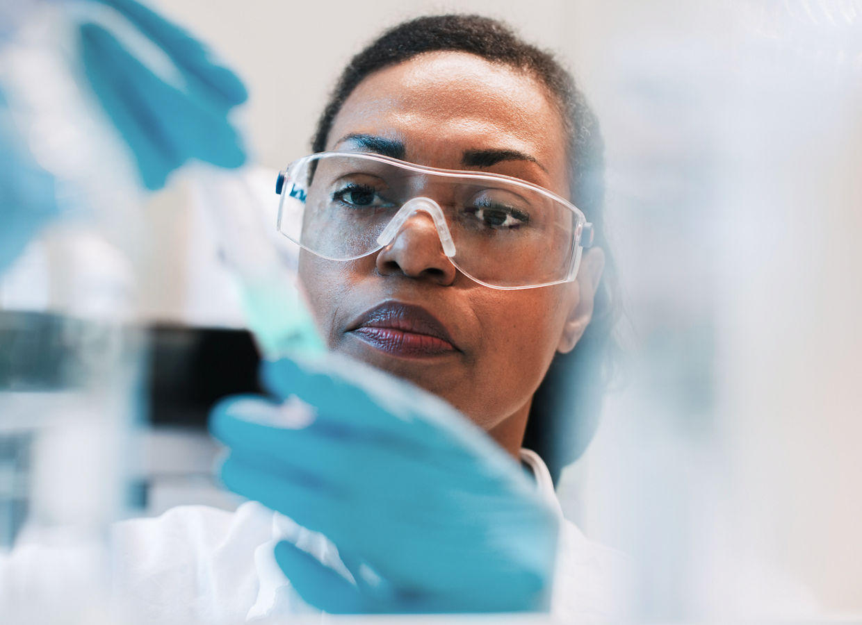 A female scientist wearing safety googles, gloves and a lab coat working on an experiment in a lab.