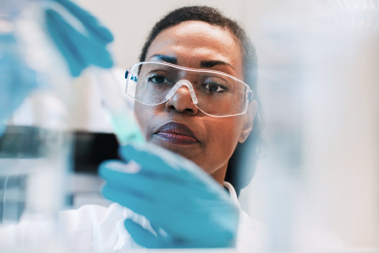A scientist wearing safety goggles, gloves and a lab coat working on an experiment in a lab.