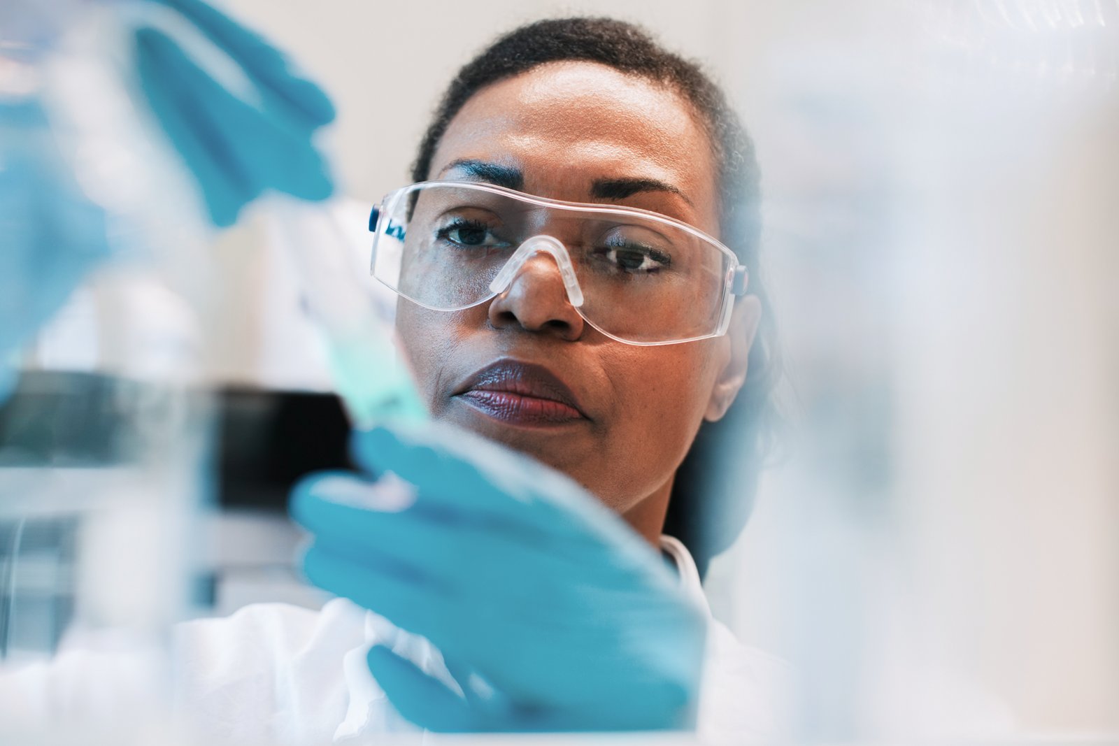 A scientist wearing safety goggles, gloves and a lab coat working on an experiment in a lab.