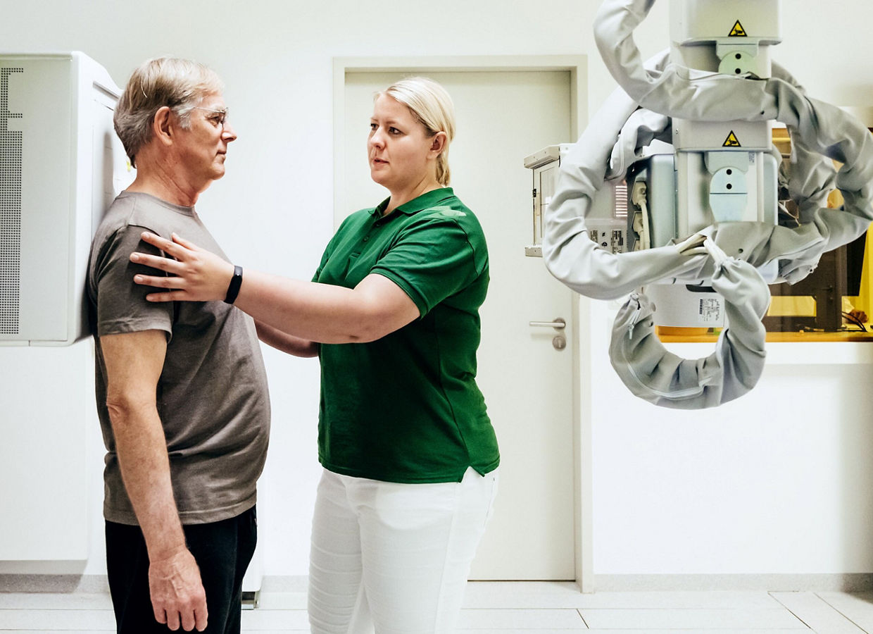 An imaging technician positioning a patient for an x-ray by touching their shoulders