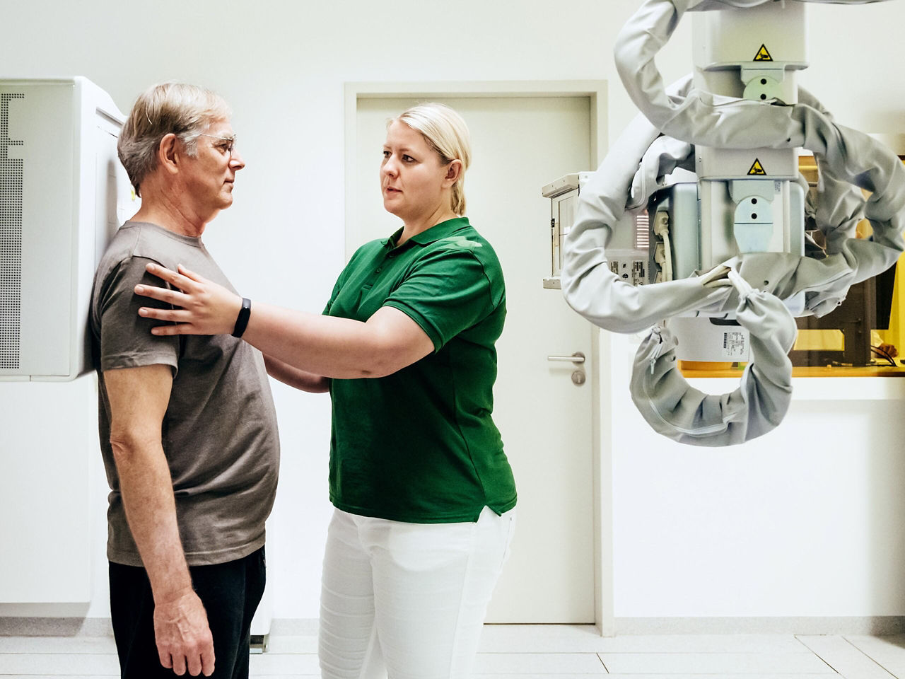 An imaging technician positioning a patient for an x-ray by touching their shoulders