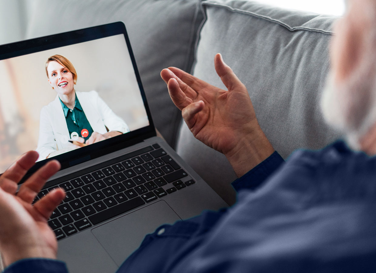 Un uomo seduto sul divano che parla con il medico durante un appuntamento di telemedicina.