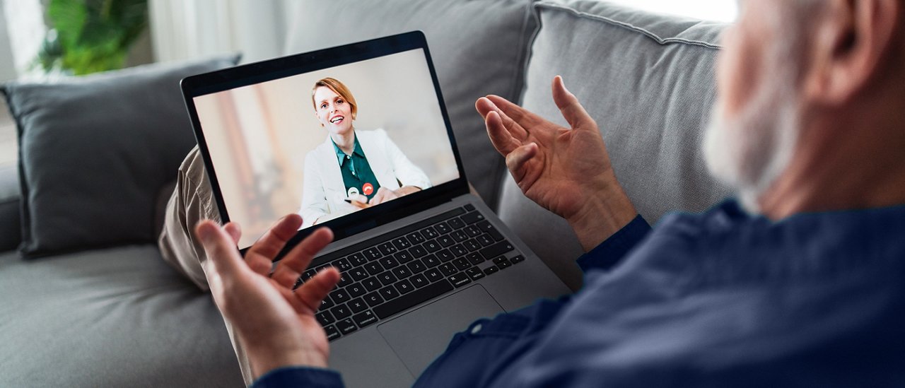 Un uomo seduto sul divano che parla con il medico durante un appuntamento di telemedicina.