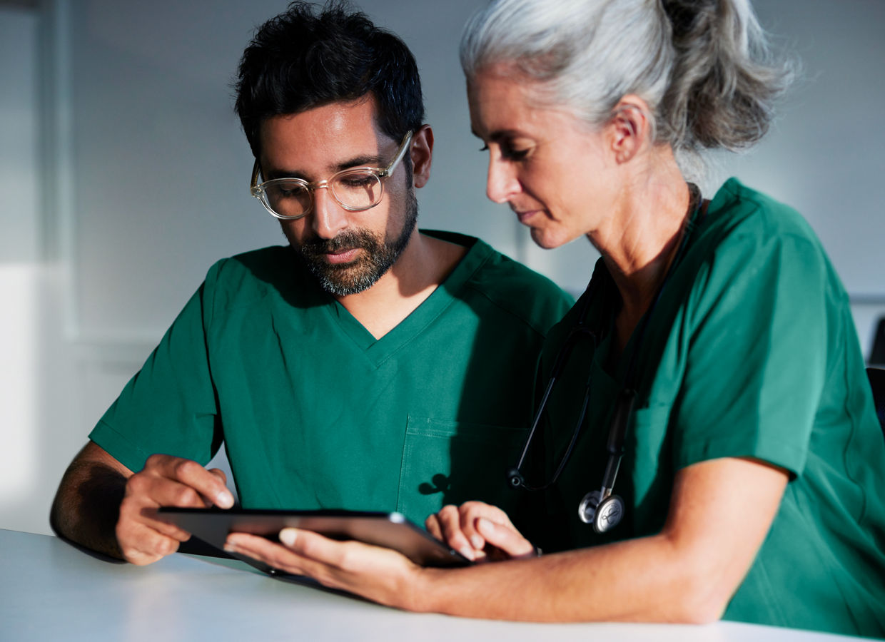 A female and male clinician both in scrubs viewing a digital tablet screen in a classroom setting.