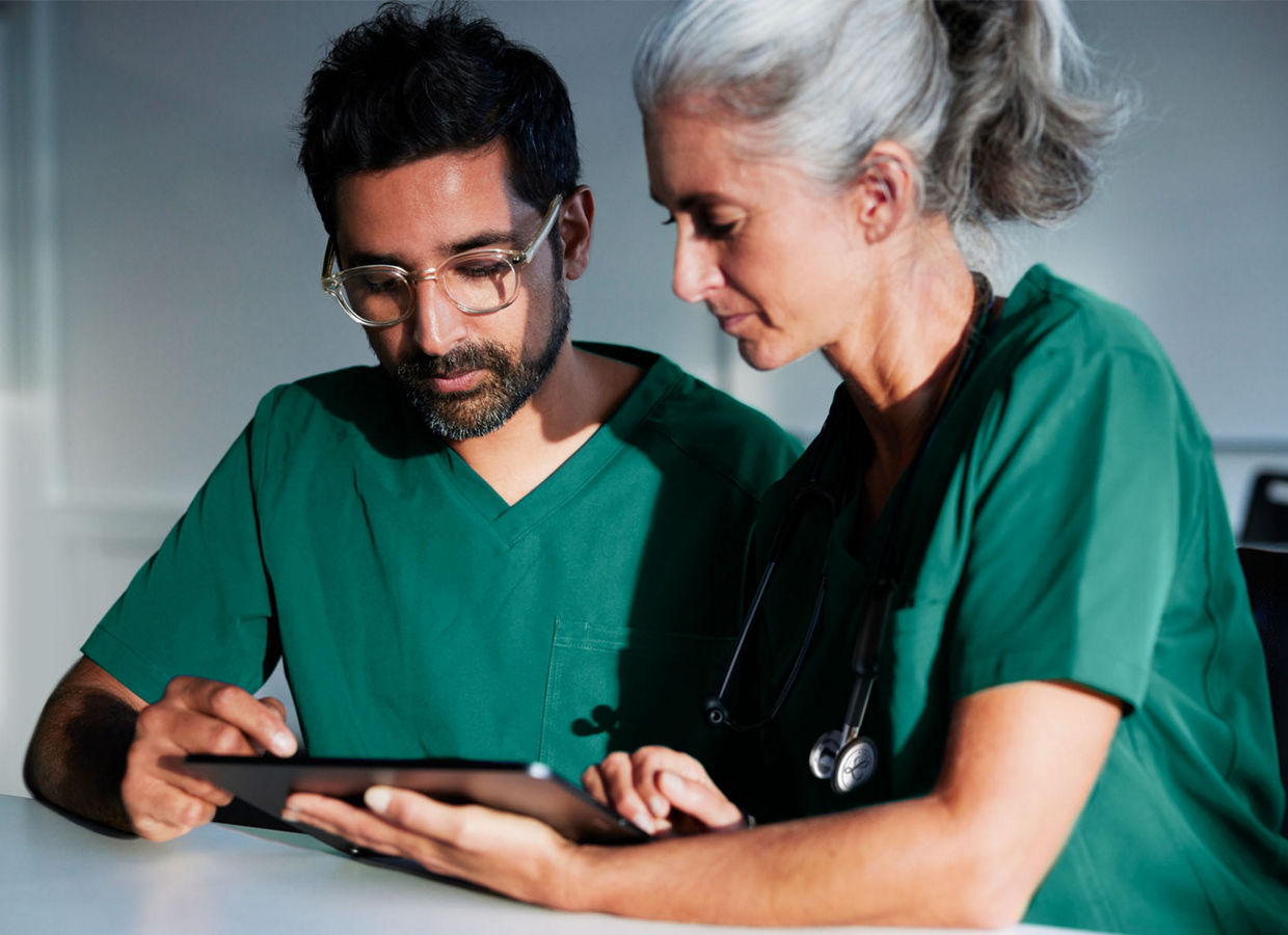 This is a Getty image that has been retouched to reflect the Solventum brand. It is an image of a female and male clinician both in scrubs viewing a digital tablet screen in a classroom setting.