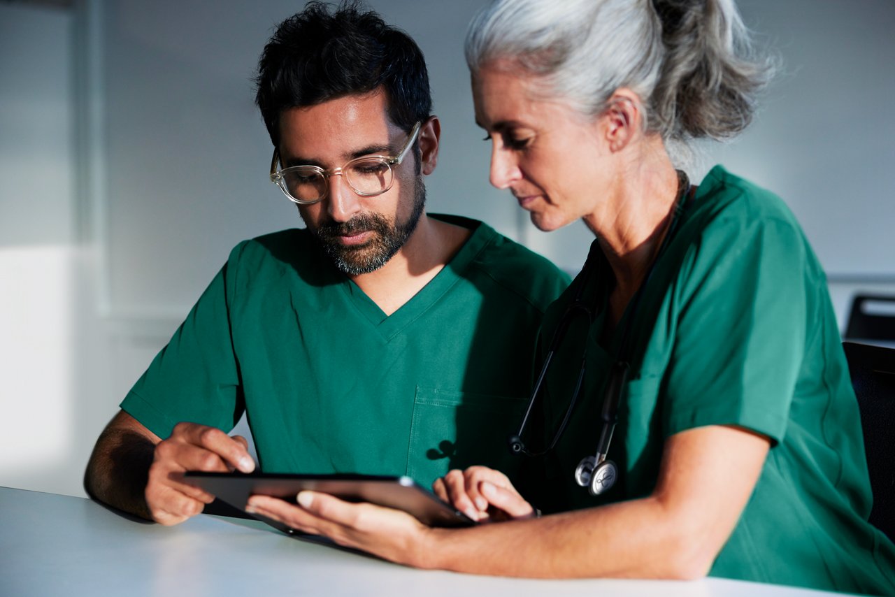 It is an image of a female and male clinician both in scrubs viewing a digital tablet screen in a classroom setting.