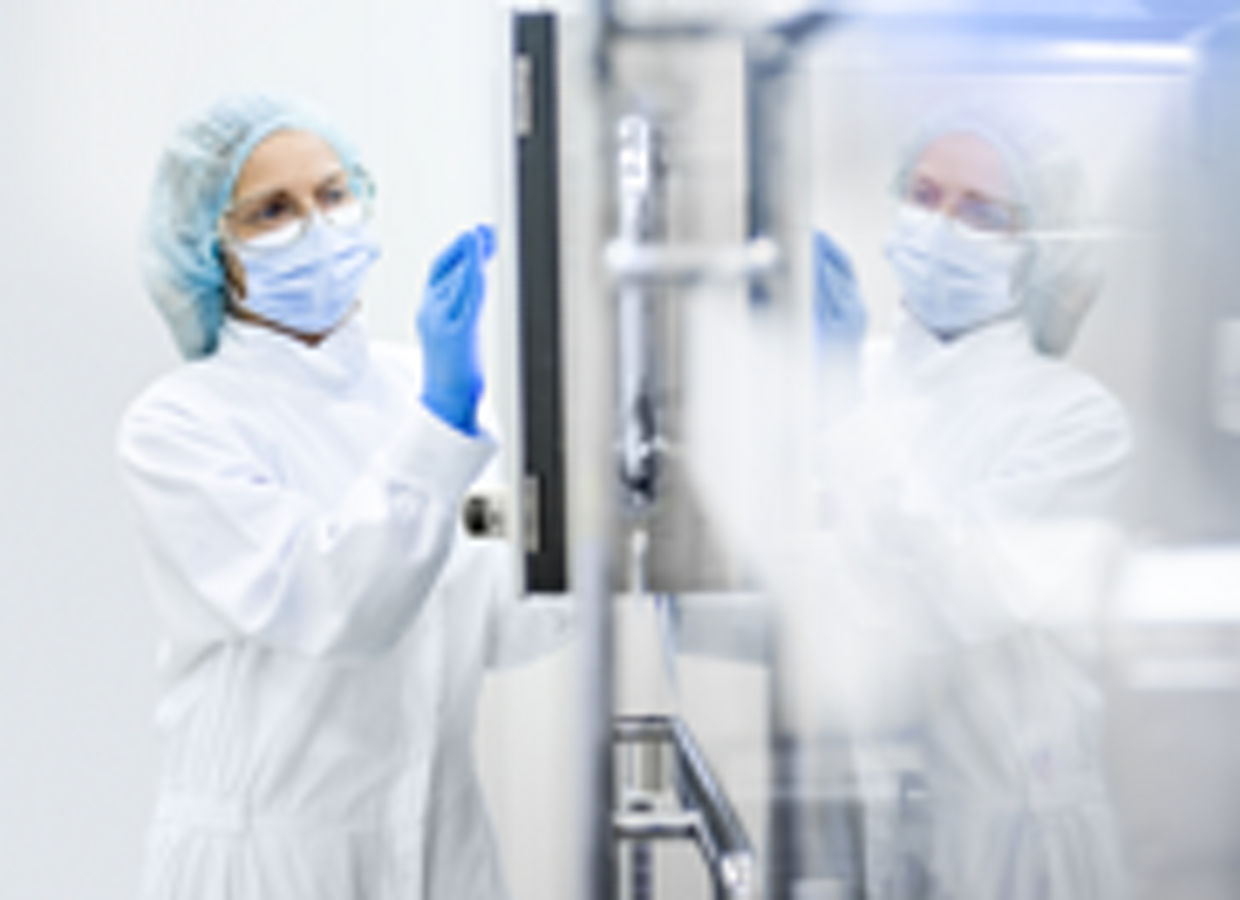 A sterile-gowned female worker in a clean room standing next to equipment and touching the screen.