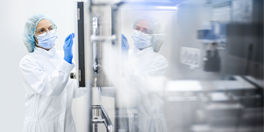 A sterile-gowned female worker in a clean room standing next to equipment and touching the screen.